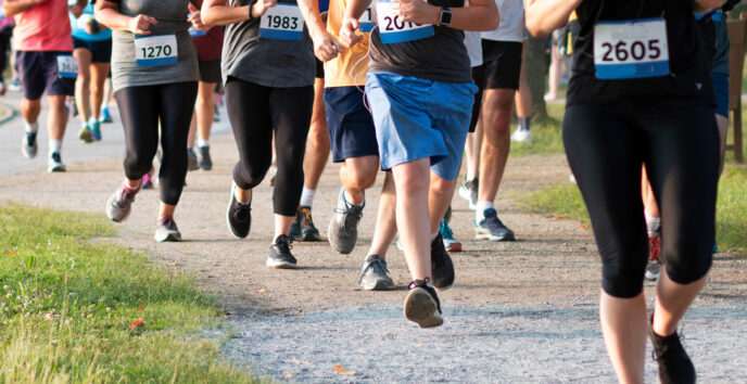 Group of runners in a race, visible bib numbers, midstride on a gravel path in a park.