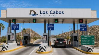 Toll booth lane at Los Cabos Toll Road with green downward arrows and a black SUV approaching the gate, desert hills in the background.