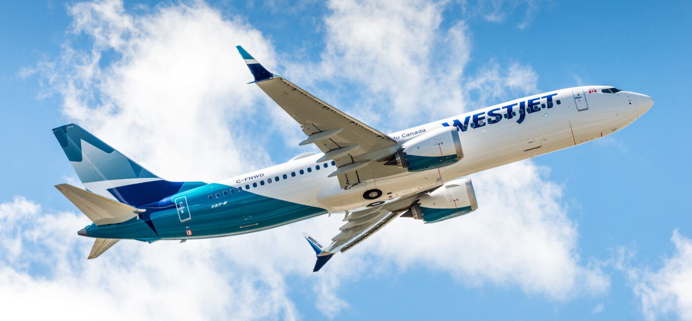 WestJet airliner in blue and white livery flying through a bright, partly cloudy sky.
