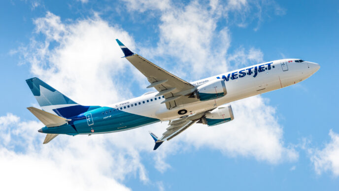WestJet airliner in blue and white livery flying through a bright, partly cloudy sky.