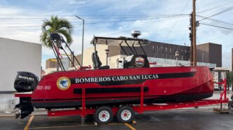 Red firefighting boat on a trailer, labeled Bomberos Cabo San Lucas, with Suzuki outboard motor and equipment on top, parked in a lot.