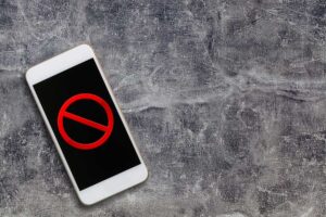 Smartphone on a rough gray surface displaying a red prohibition (no) symbol on the screen