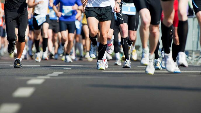 AdobeStock_64258895 - Gringo Gazette Group of runners in colorful athletic gear sprinting on a road, race bibs visible on their chests/waists.