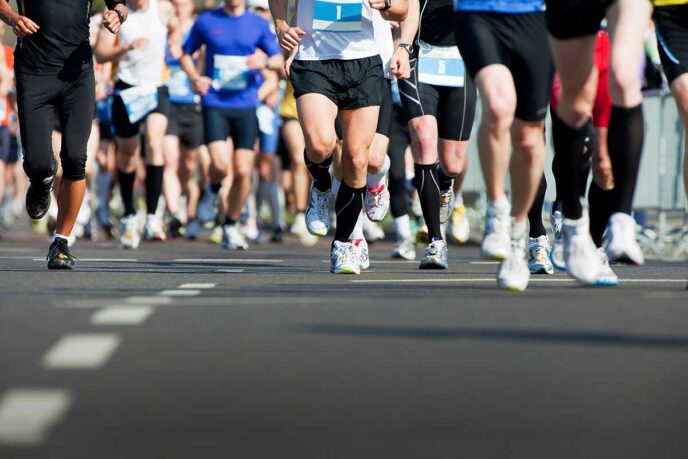 AdobeStock_64258895 - Gringo Gazette Group of runners in colorful athletic gear sprinting on a road, race bibs visible on their chests/waists.