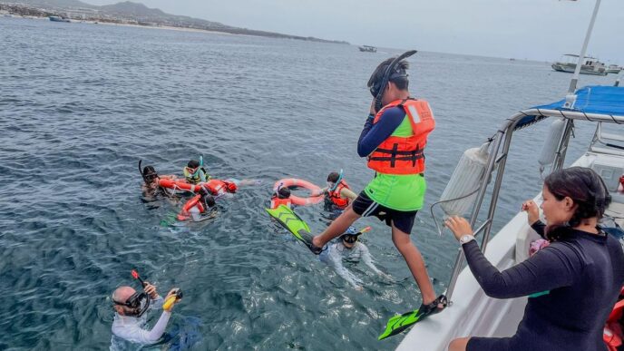 Group of people snorkeling from a boat, wearing life jackets and fins, in clear water near shore with a Mexican flag on board.