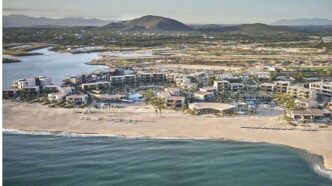 Aerial view of a beachfront resort with white buildings along a sandy shore and turquoise ocean coast.