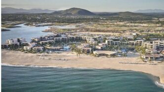 Aerial view of a beachfront resort with white buildings along a sandy shore and turquoise ocean coast.