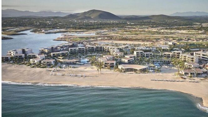 Aerial view of a beachfront resort with white buildings along a sandy shore and turquoise ocean coast.