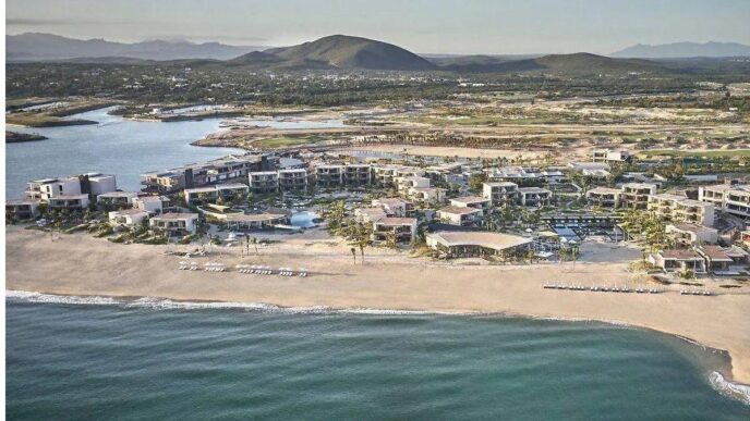 Aerial view of a beachfront resort with white buildings along a sandy shore and turquoise ocean coast.