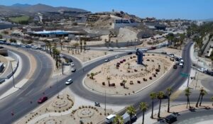 Aerial view of a large roundabout with a tall blue sculpture at the center, desert landscaping and palm trees along the roads.