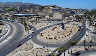 Aerial view of a large roundabout with a tall blue sculpture at the center, desert landscaping and palm trees along the roads.