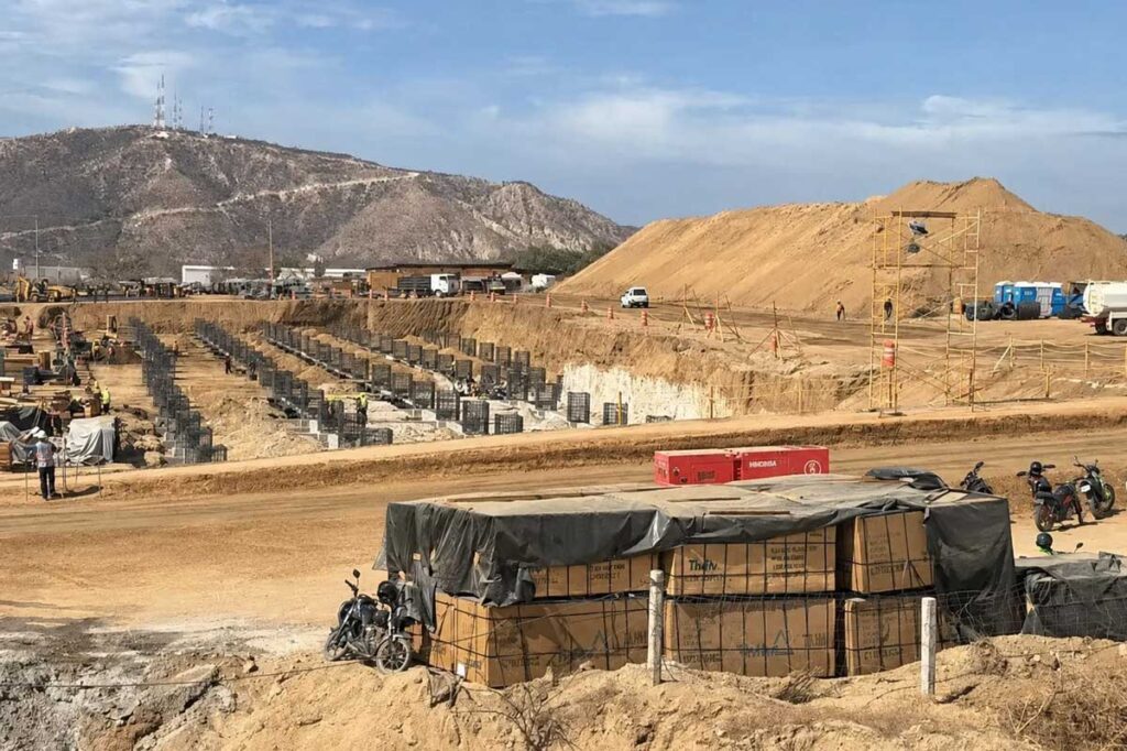 Construction site with multiple vertical formwork pillars set in rows for foundational work, brown dirt, and distant hills under a blue sky