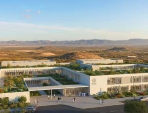Modern white campus-style buildings with rooftop gardens in a desert landscape, hills in the distance, people walking outside.