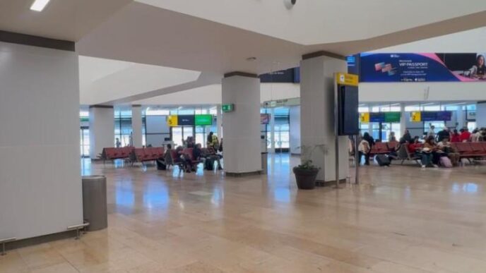 Open airport terminal with rows of pink seats and passengers waiting near gates in the background.