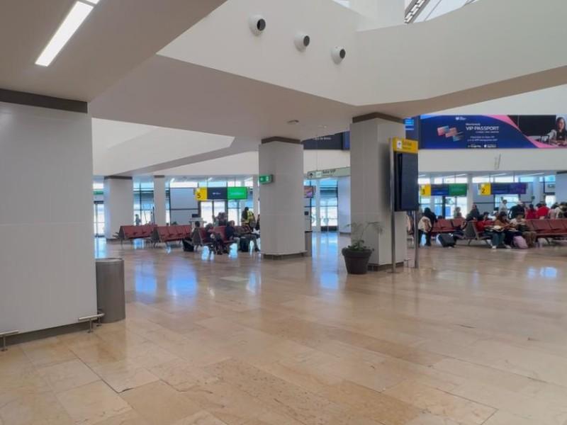 Open airport terminal with rows of pink seats and passengers waiting near gates in the background.