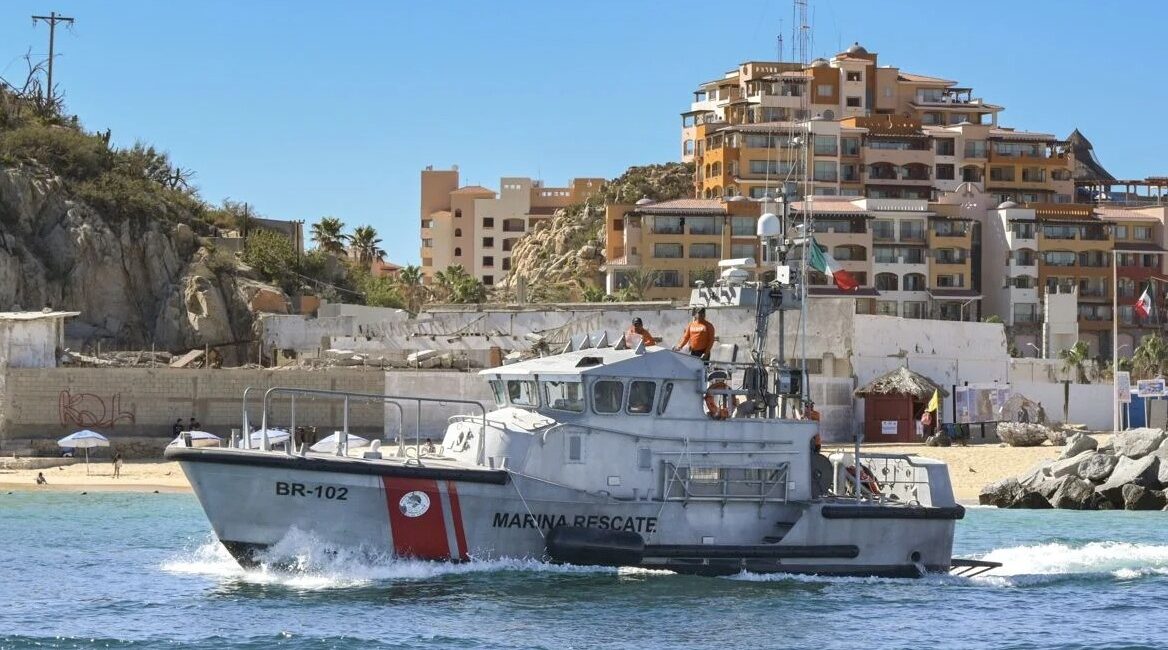 Rescue boat on calm blue water near a sandy beach with apartment buildings in the background