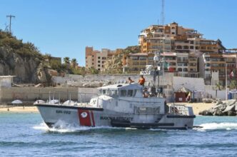 Rescue boat on calm blue water near a sandy beach with apartment buildings in the background