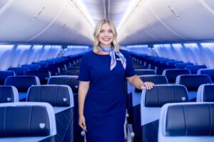 Flight attendant in a blue uniform standing in an airplane cabin with blue seats behind her in a modern jet.
