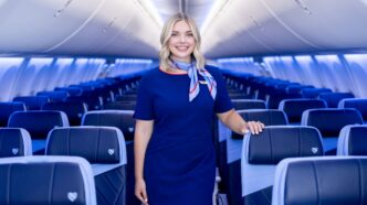 Flight attendant in a blue uniform standing in an airplane cabin with blue seats behind her in a modern jet.