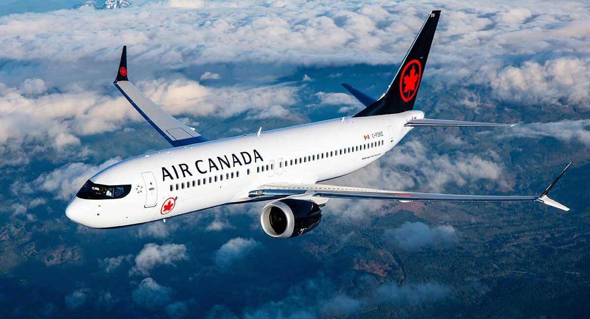 Air Canada passenger jet flying above clouds, white fuselage with red maple leaf logo on tail. It’s a side view with engines under the wing.