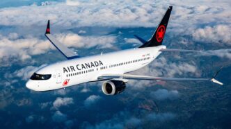 Air Canada passenger jet flying above clouds, white fuselage with red maple leaf logo on tail. It’s a side view with engines under the wing.