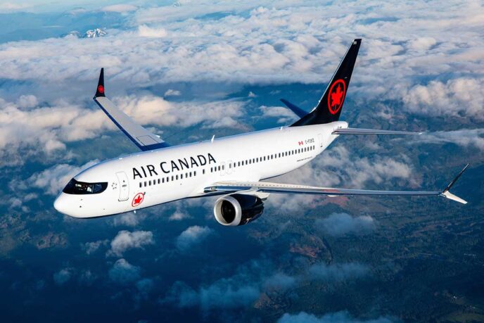 Air Canada passenger jet flying above clouds, white fuselage with red maple leaf logo on tail. It’s a side view with engines under the wing.