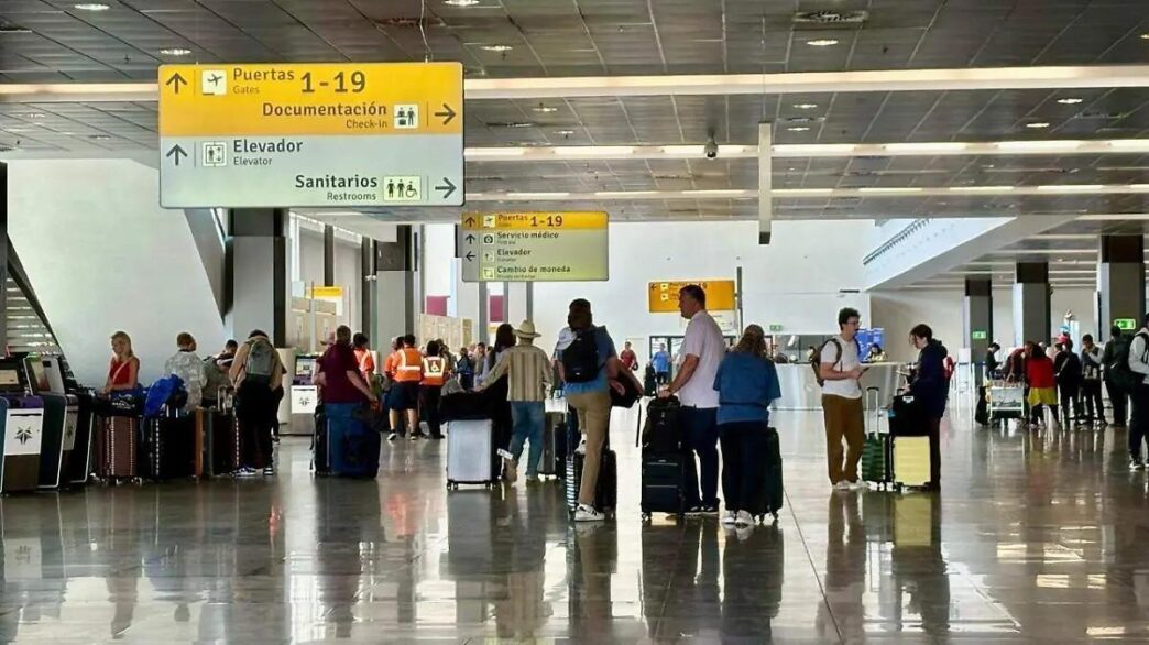 Busy airport terminal with travelers and rolling suitcases under overhead signs pointing to gates 1–19, documentation, restrooms and elevators.