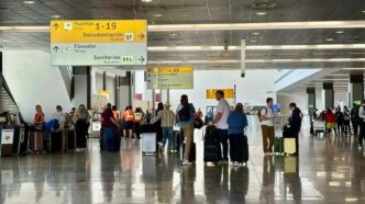 Busy airport terminal with travelers and rolling suitcases under overhead signs pointing to gates 1–19, documentation, restrooms and elevators.