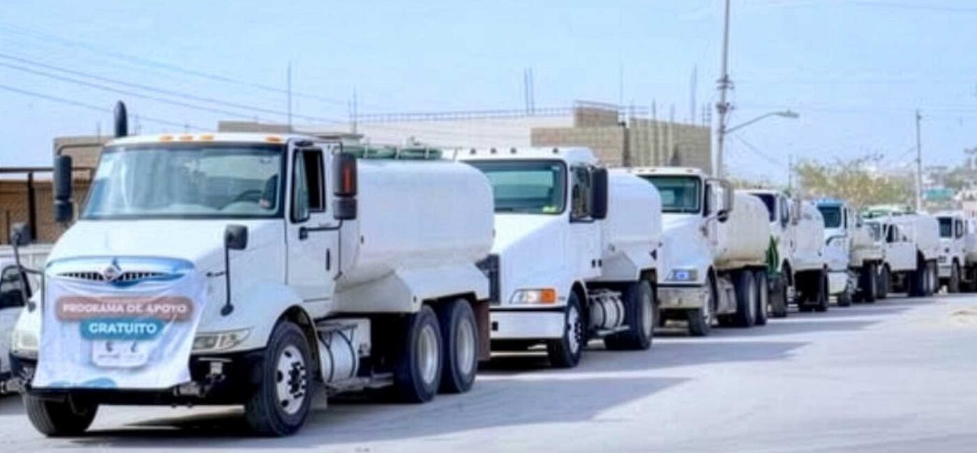 laPipa - Gringo Gazette Line of white delivery trucks driving in a convoy down a city street under a clear sky.