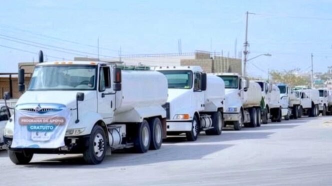laPipa - Gringo Gazette Line of white delivery trucks driving in a convoy down a city street under a clear sky.