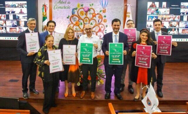 Ten people in business attire stand on a stage, each holding a certificate of achievement in different colors, with a decorative mural behind.