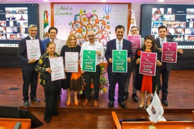 Ten people in business attire stand on a stage, each holding a certificate of achievement in different colors, with a decorative mural behind.