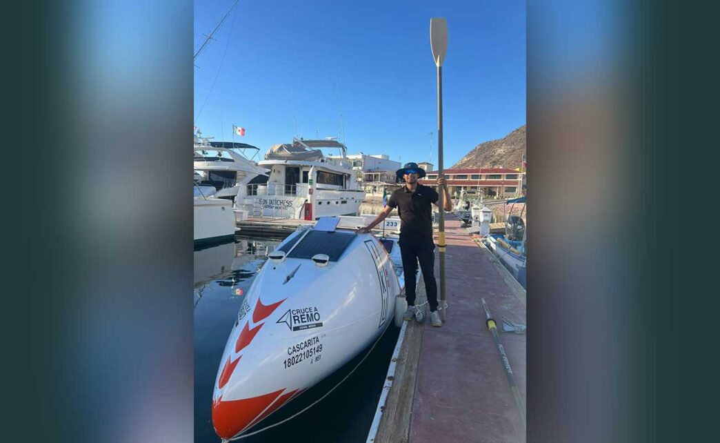 Person standing on a dock next to a white speedboat with a paddle raised beside them at a marina.