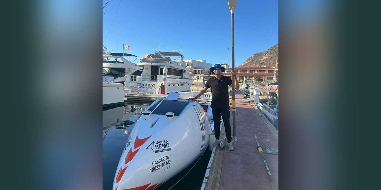 Person standing on a dock next to a white speedboat with a paddle raised beside them at a marina.
