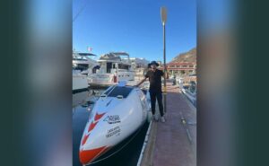 Person standing on a dock next to a white speedboat with a paddle raised beside them at a marina.