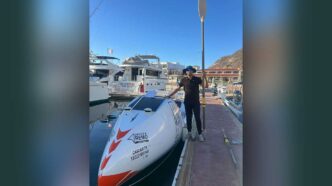 Person standing on a dock next to a white speedboat with a paddle raised beside them at a marina.