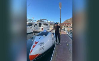 Person standing on a dock next to a white speedboat with a paddle raised beside them at a marina.
