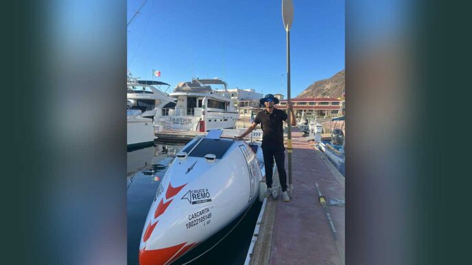 Person standing on a dock next to a white speedboat with a paddle raised beside them at a marina.
