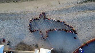Aerial view of a group of people standing together on a sandy beach, forming a large star-shaped outline.