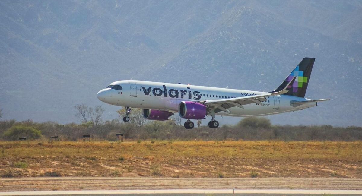 Volaris passenger jet lifting off the runway with desert vegetation and mountains in the background.