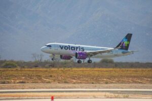 Volaris passenger jet lifting off the runway with desert vegetation and mountains in the background.
