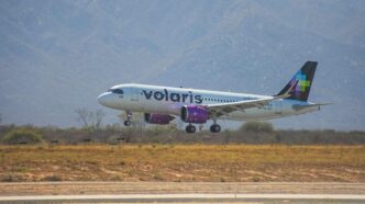 Volaris passenger jet lifting off the runway with desert vegetation and mountains in the background.
