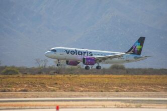 Volaris passenger jet lifting off the runway with desert vegetation and mountains in the background.