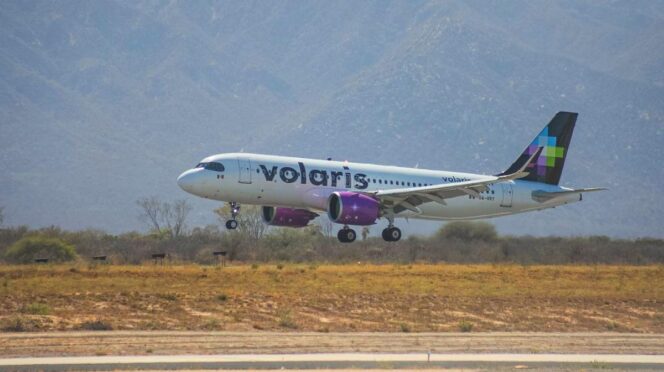 Volaris passenger jet lifting off the runway with desert vegetation and mountains in the background.