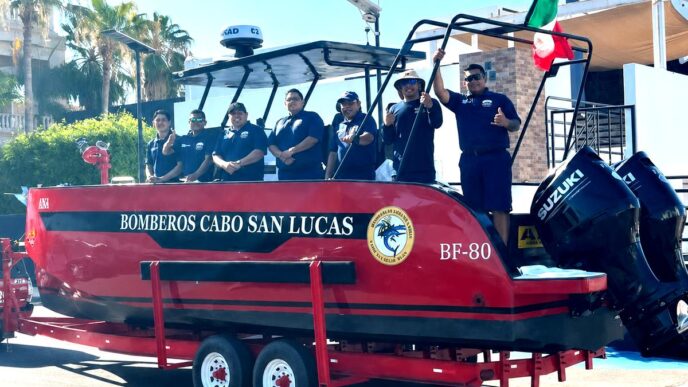 Red rescue boat on a trailer with six firefighters in navy shirts, Cabo San Lucas fire department, Mexico flag raised nearby.