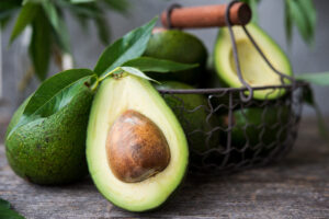 Halved avocado with a large brown seed, placed in a rustic basket on a wooden surface