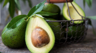Halved avocado with a large brown seed, placed in a rustic basket on a wooden surface