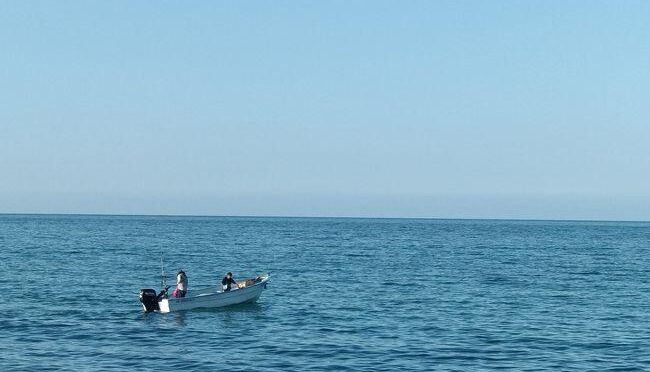 Small motorboat with two people sailing on a calm blue sea under a clear sky.