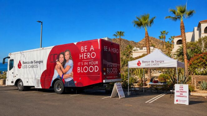 Blood donation truck with 'Be a Hero' message, and a tent for a blood bank outreach at a sunny parking lot in Los Cabos
