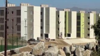 Casas-Bienestar - Gringo Gazette Row of modern white and light-green apartment buildings under construction, with a dirt street and boulders in the foreground.